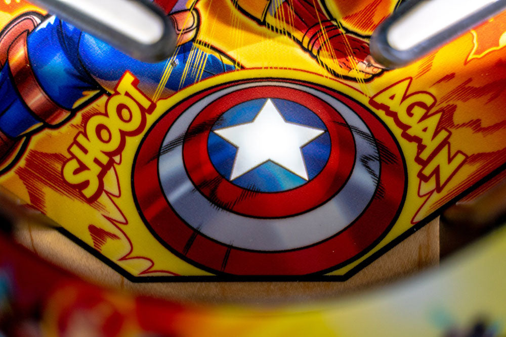 Close-up of a Captain America shield on a colorful background with 'Shoot Again' text.