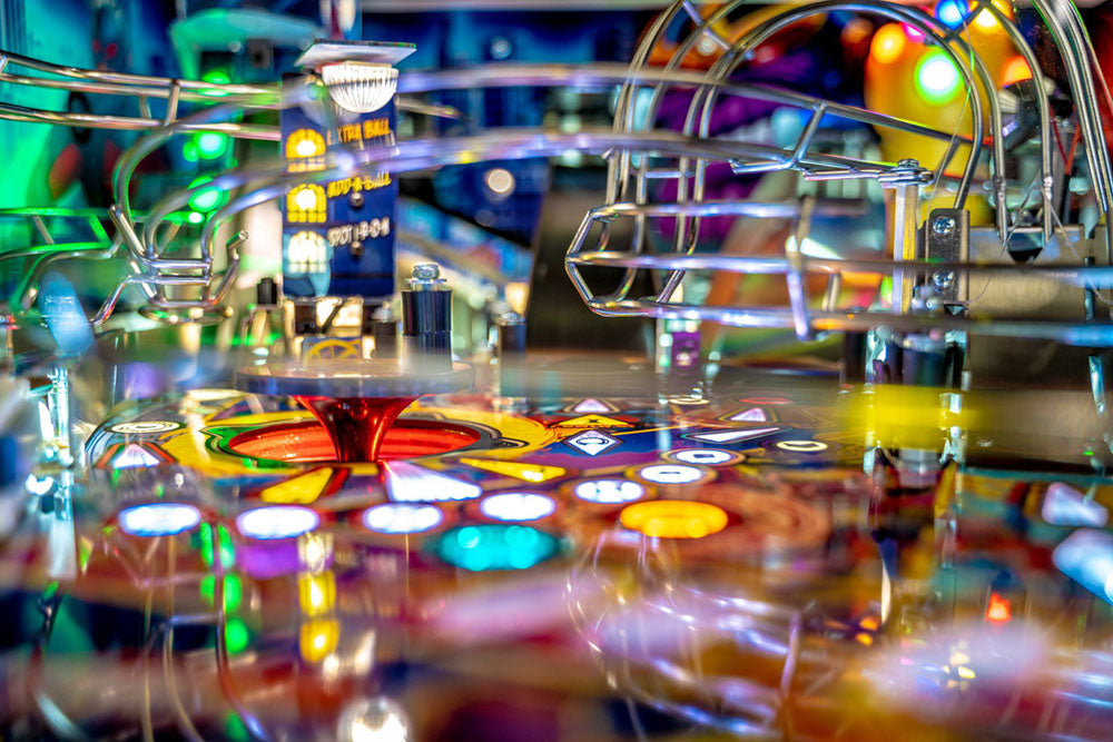 Close-up of a pinball machine with colorful lights and reflections.