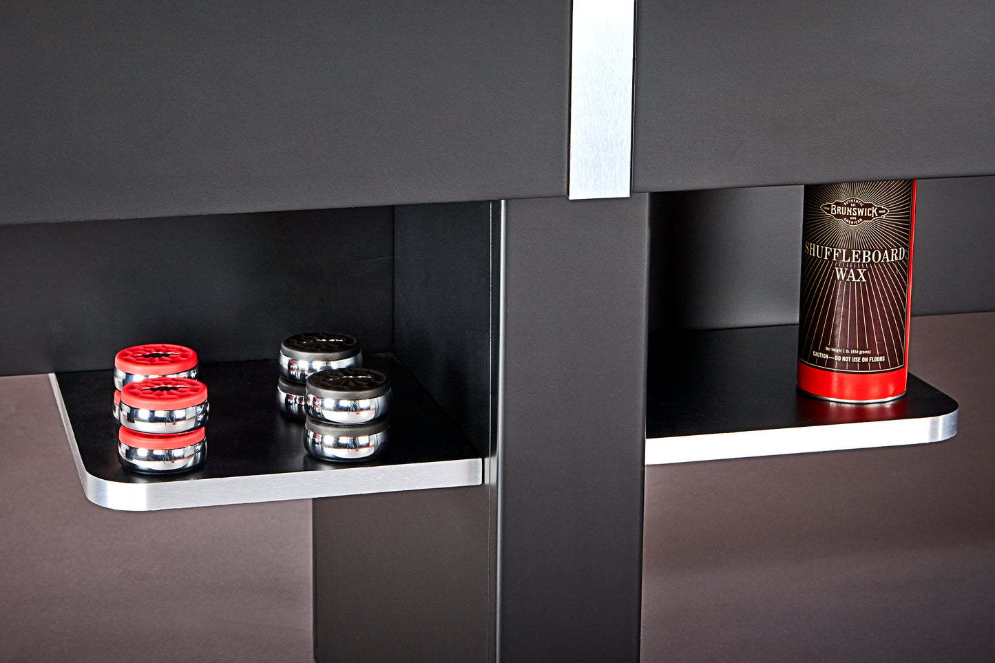 Black shelving under a shuffleboard table with red and silver items on a grey background.