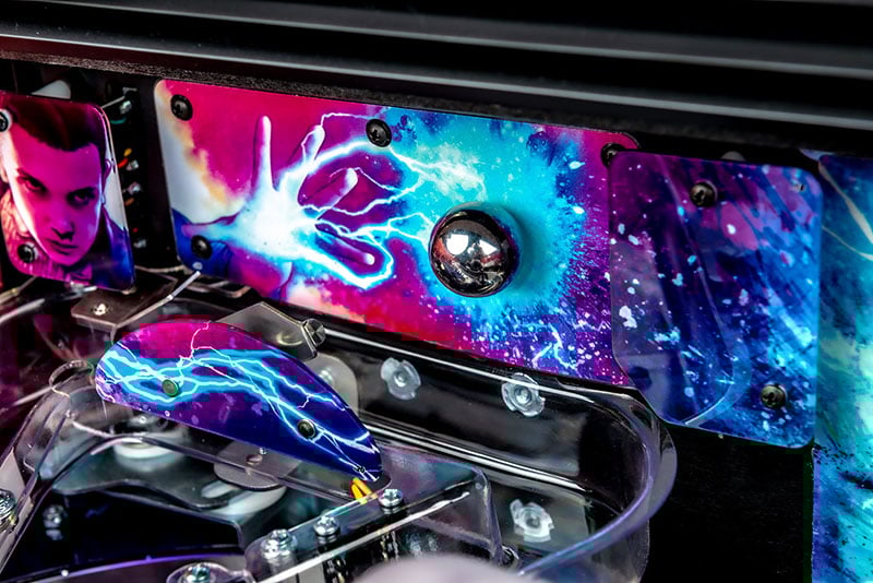 Close-up of a colorful pinball machine playfield with neon lights and mechanical components.