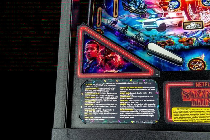 Close-up of a pinball machine with a character portrait and text panel, featuring Netflix branding.