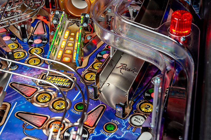 Close-up of a pinball machine with colourful playfield and red light.