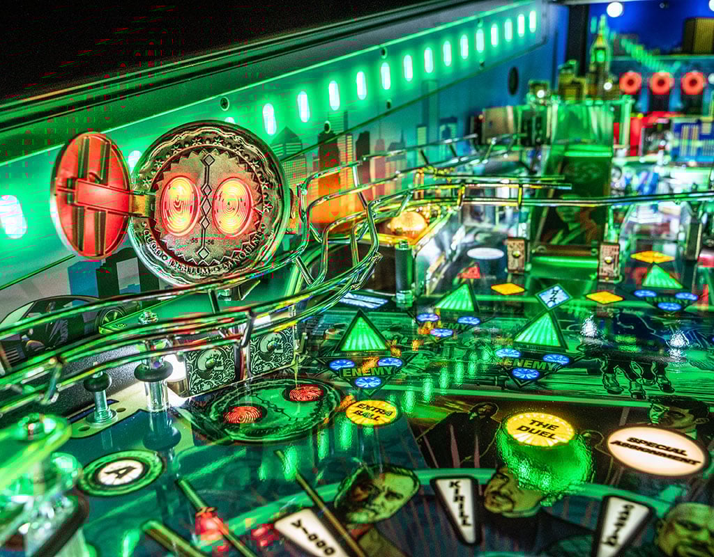 Close-up of a pinball machine with vibrant green and red lights.