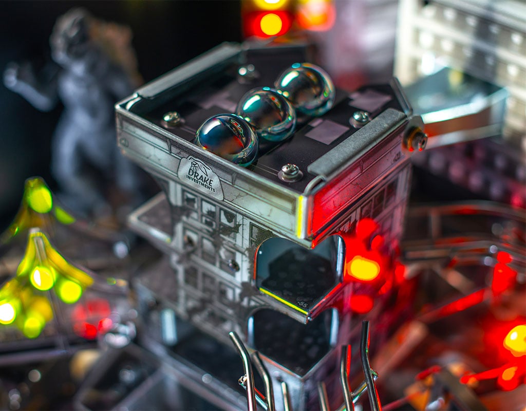 Close-up of a pinball machine with detailed components and lights, set against a blurred background.